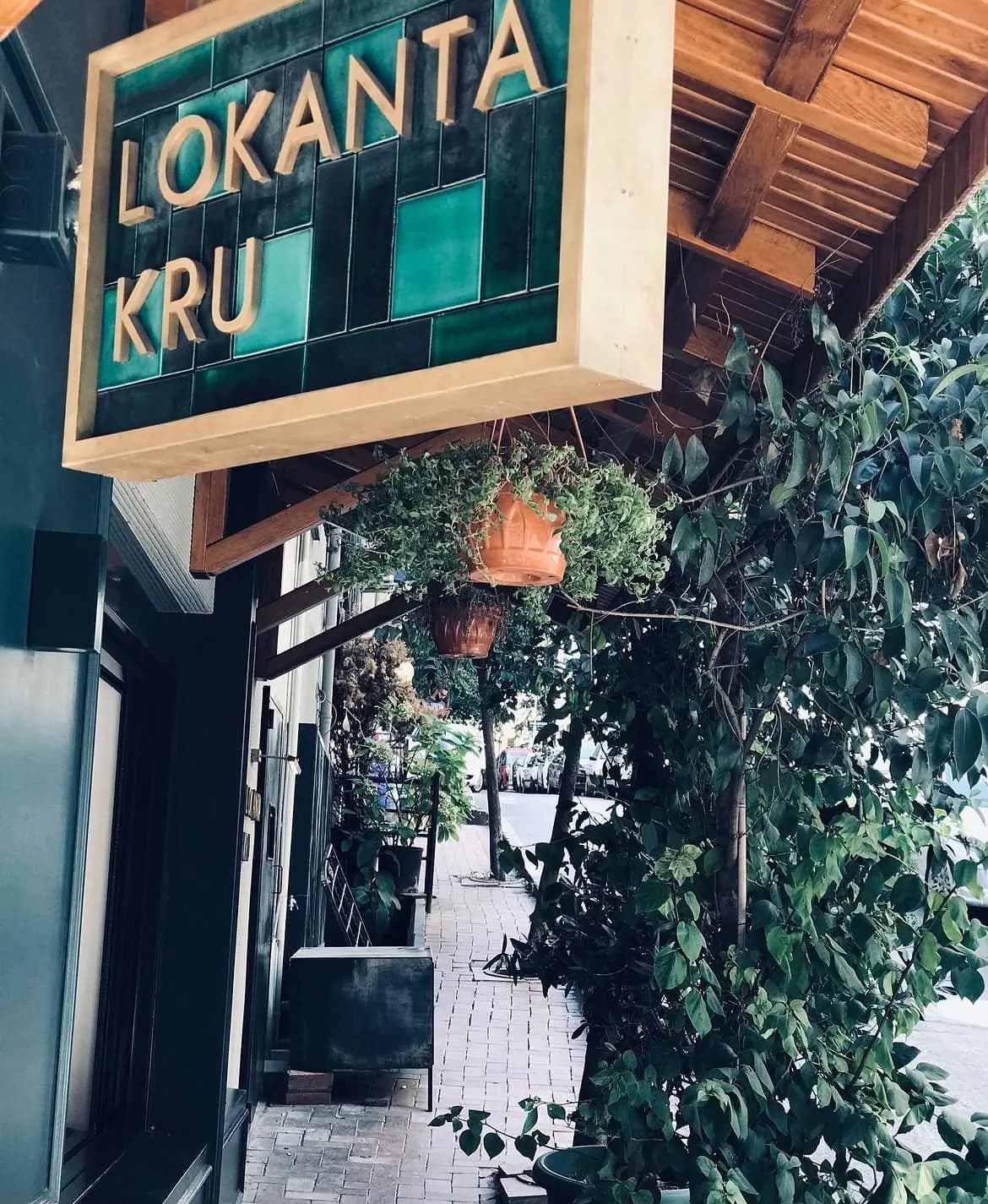 Lokanta Kru'nun yeşil çinili, altın harfli dış tabelası; ahşap saçak, sarmaşık ve terrakota saksılar.