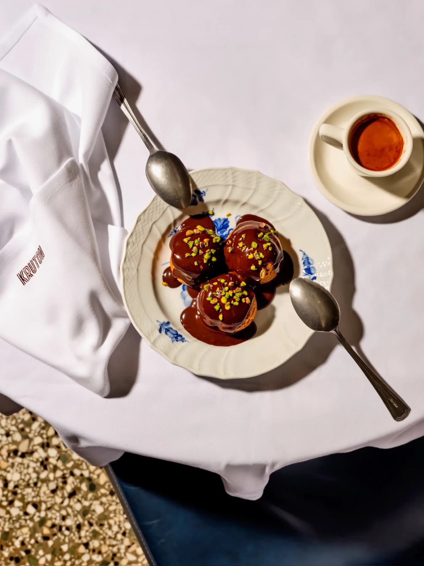 Çikolata soslu profiterol ve yanında espresso; altında KRUTON işlemeli beyaz peçete.